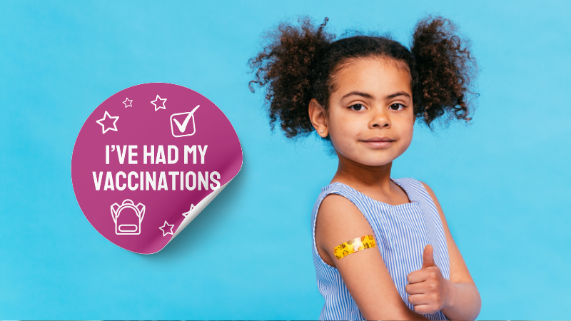 Young girl looking at the camera with her thumb up. She has a yellow sticker on her arm. Next to her is a big purple sticker that says "I've had my vaccinations".