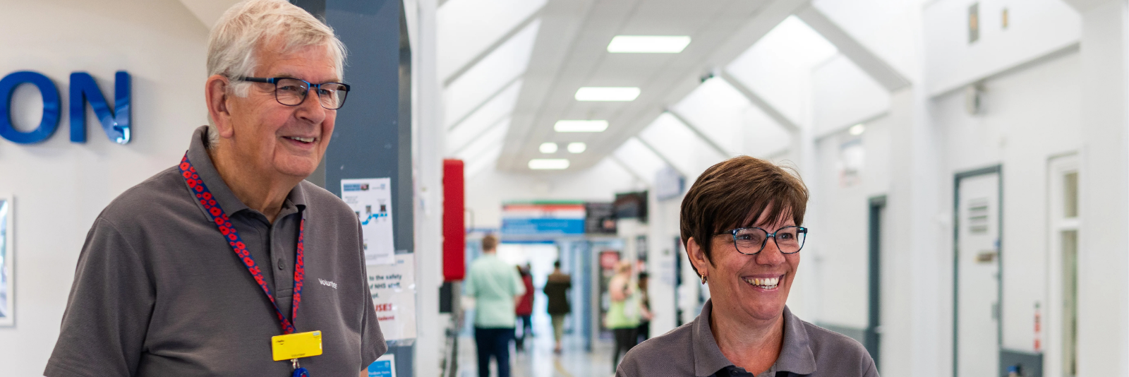 Two volunteers smiling as they great people at a hospital